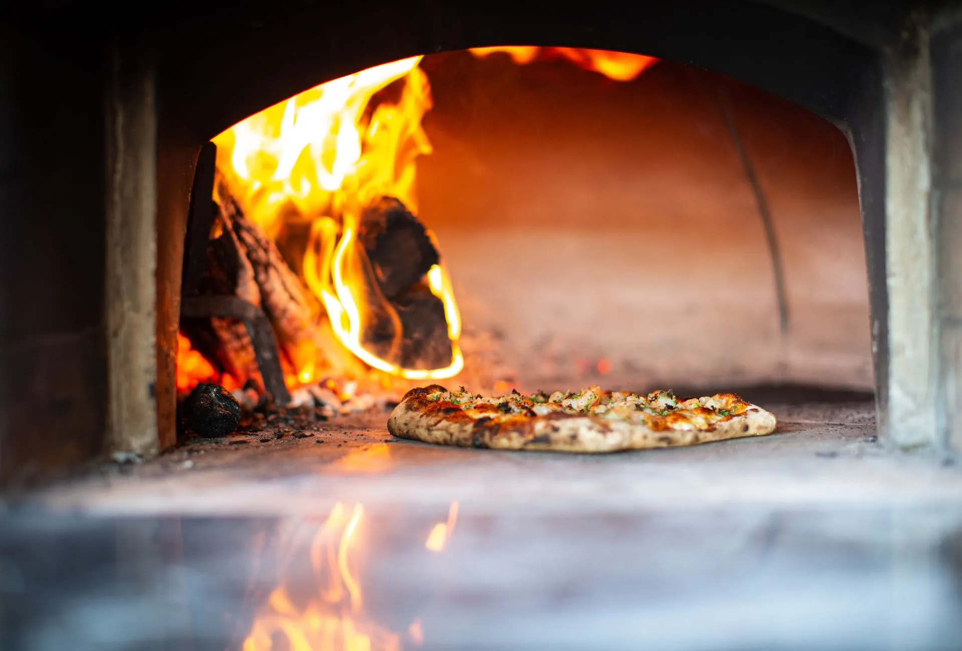 Pizza assando no forno a lenha, com a chama ao fundo